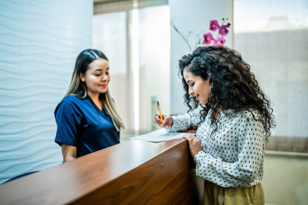 Mid adult woman talking with receptionist at the reception desk of the dentist's office Front Desk Training