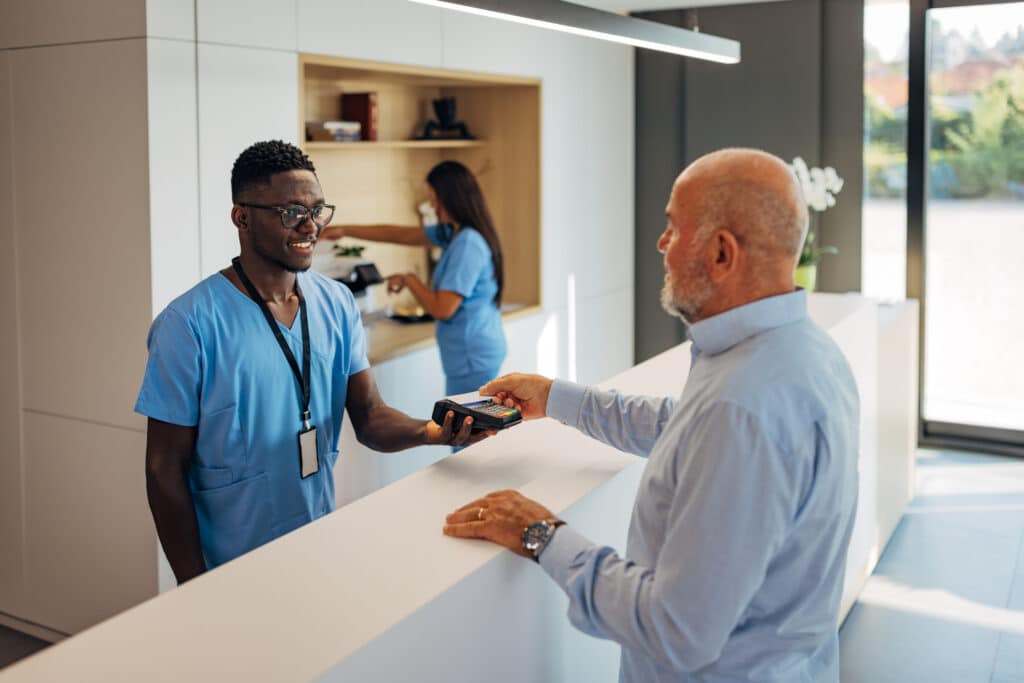 Senior male patient making payment using credit card contactless with a credit card reader machine in modern clinic. NFC technology Payment Processing